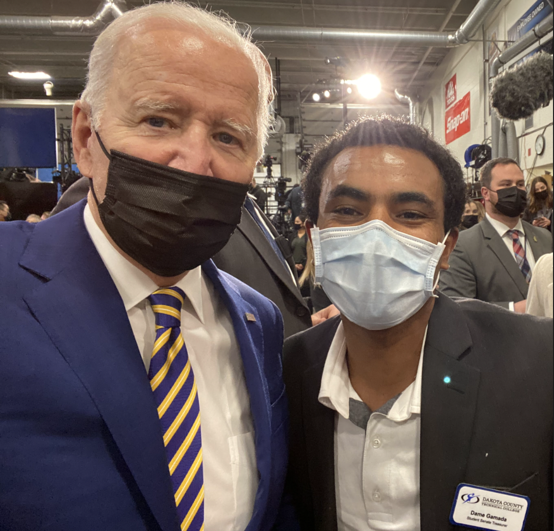 Dame Gamada poses for a photo with Joe Biden. Both men are wearing surgical masks and suits.