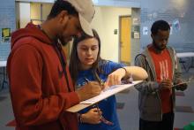 Student with clipboard filling out their registration while another student helps