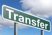 Image of a green street sign that says "Transfer" in front of a blue sky with clouds.